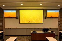 Primary projection screen with display screens mounted to left and right so that students will be able to see remote participants without having to turn to look at the projection screen