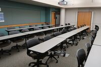 Back of room view of student table and chair seating and  exit door at rear right of room