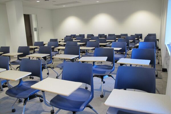 Rear of room view of student tablet arm chair seating on casters and exit door on left side of room