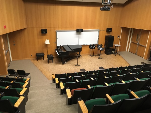 Photo of front of room from back of room with auditorium seating and piano at front.