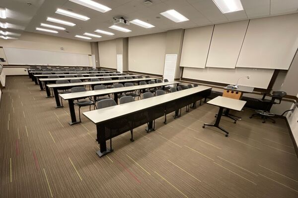 Back of room view of student tables and chairs and markerboard on rear wall