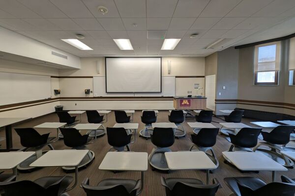 Front of room view with lectern on right in front of markerboard and projection screen lowered