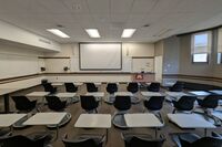 Front of room view with lectern on right in front of markerboard and projection screen lowered