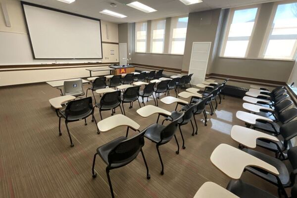 Front of room view with lectern on right in front of markerboard and projection screen lowered