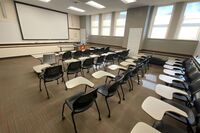 Front of room view with lectern on right in front of markerboard and projection screen lowered