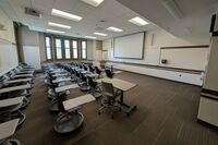 Front of room view with lectern on left in front of markerboard and projection screen partially lowered