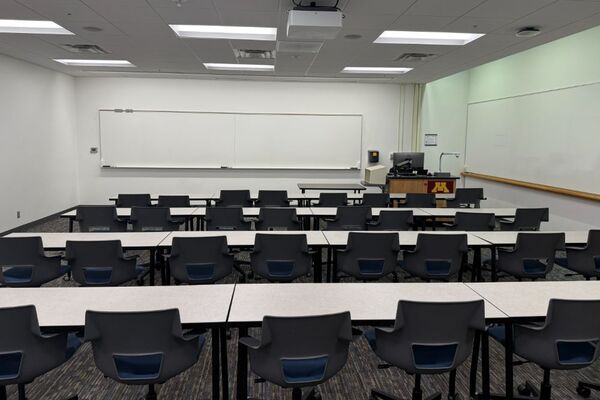 Front of room view with lectern on right in front of markerboard and projection screen lowered