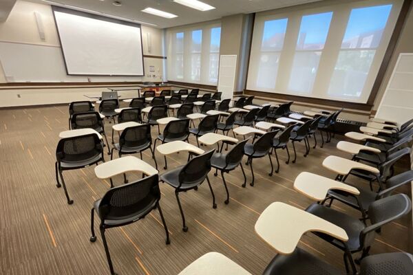 Front of room view with lectern on right in front of markerboard and projection screen partially lowered