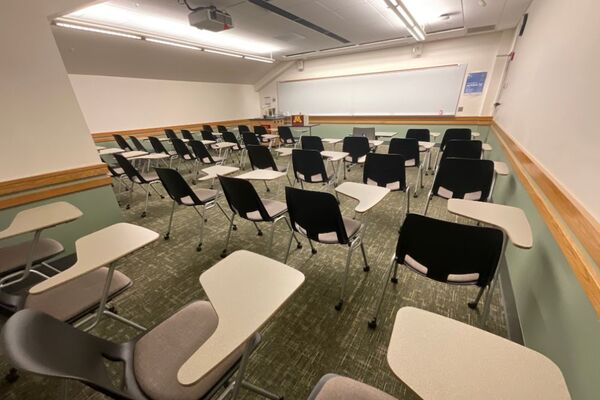 Front of room view with lectern on left in front of markerboard and projection screen raised