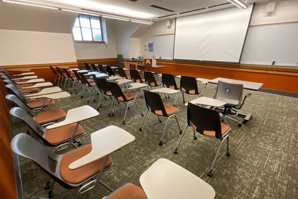 Front of room view with lectern on left in front of markerboard and projection screen lowered