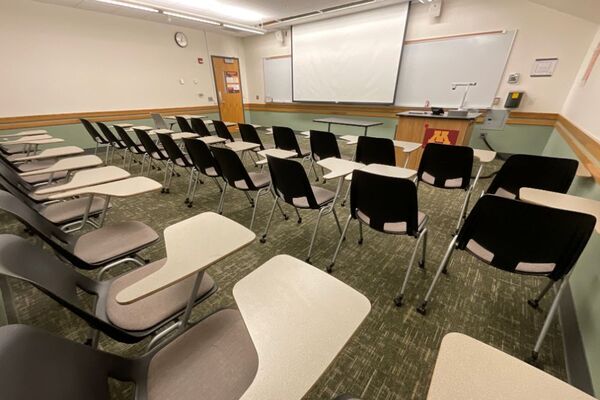 Front of room view with lectern on right in front of markerboard and projection screen lowered
