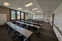 Front of room view with lectern on left in front of markerboard and projection screen partially lowered