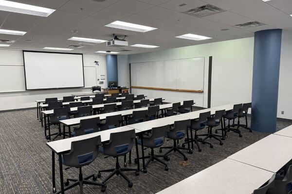 Front of room view with lectern on right in front of markerboard, screen lowered