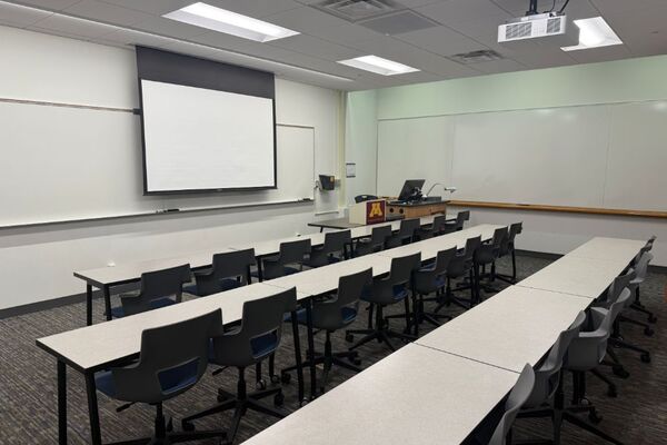 Front of room view with lectern on right in front of markerboard and projection screen lowered