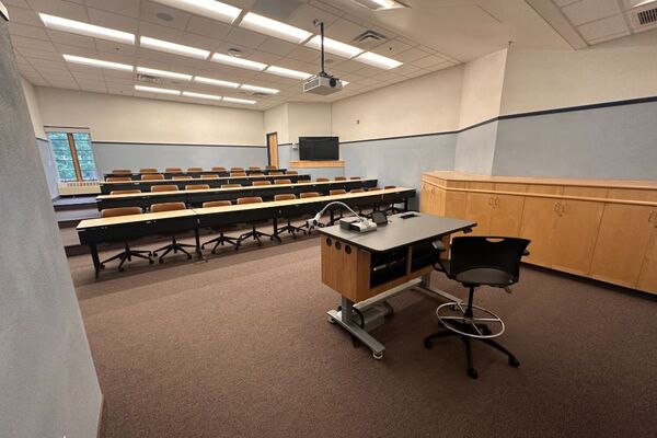 Back of room view of student tiered table and chair seating and display monitor on right rear wall