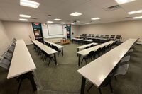  Front of room view with lectern center, exit doors left and right, and projection screen lowered in front of markerboard
