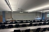 Back of room view of student tiered fixed-table and chair seating and exit doors at left and right rear of room