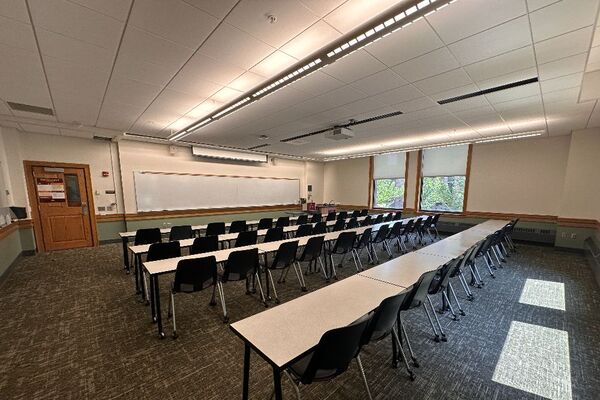 Front of room view with lectern on right in front of markerboard and projection screen lowered