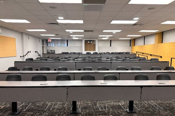 Back of room view of student fixed-table and chair seating and exit door at left rear of room