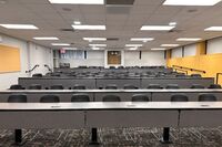 Back of room view of student fixed-table and chair seating and exit door at left rear of room