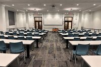 Front of room view with projection board lowered, lectern in front of markerboard, and exit doors to left and right