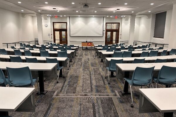 Front of room view with projection board lowered, lectern in front of markerboard, and exit doors to left and right