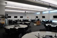Room view of student active learning round table and chair seating, markerboards and student display monitors on all walls