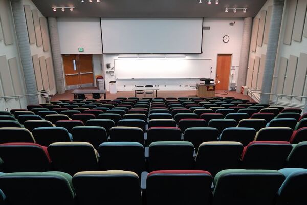 Front of room view with lectern on right in front of markerboard and projection screen lowered, double exit doors at front left of room