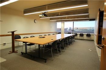Photo from doorway showing conference room table and chairs with windows at back of room.