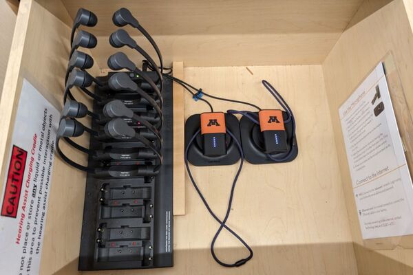 Pedestal - inside view of drawer showing two wireless mics in charging base, and assistive listening devices in charger