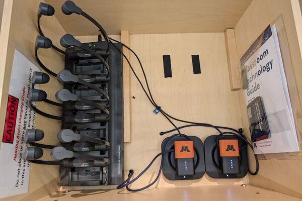 Pedestal - inside view of drawer showing two wireless mics in charging base, and assistive listening devices in charger