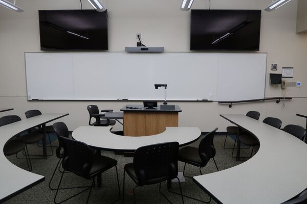 Front of room view with lectern center in front of markerboard, camera above, and display monitors to left and right 