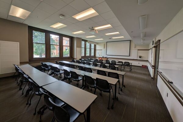 Front of room view with lectern on left in front of markerboard and projection screen partially lowered