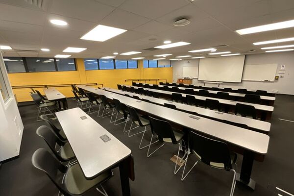 Front of room view with lectern on left in front of markerboard and projection screen lowered