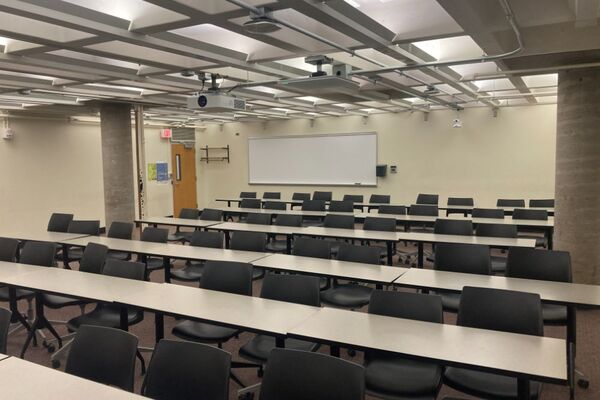 Back of room view of student table and chair seating and markerboard at rear of room, exit door on left side