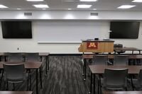Front of room view with lectern on right in front of markerboard and display screens to left and right
