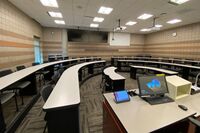 Back of room view of student tiered fixed table and chair seating and dual confidence monitors 
