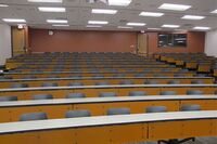 Back of room view of student tiered fixed table and chair seating, exit doors on right and left, and A/V booth on right