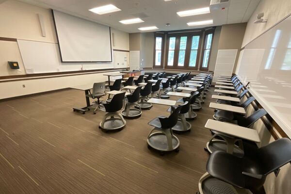 Front of room view with lectern on right in front of markerboard, screen lowered