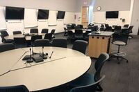 View of student collaborative table and chair seating and exit door at rear of room, side of lectern to the right