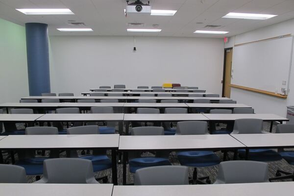 Back of room view of student table and chair seating and exit door at right rear of room