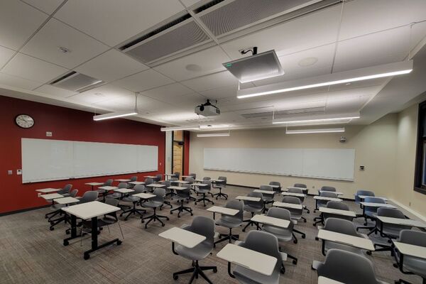 Back of room view of student tablet arm seating and markerboards on side and rear walls, exit door at left rear of room