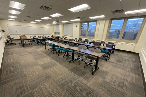 Back of room view of student table and chair seating and side markerboard on left wall of room