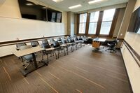 Back of room view of student tablet arm seating, confidence monitor, camera, and markerboard at rear of room