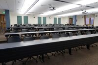 Back of room view of student tiered fixed-table and chair seating and exit doors at left and right rear of room