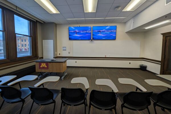 Front of room view with lectern on left in front of display, wall mounted camera, and markerboard