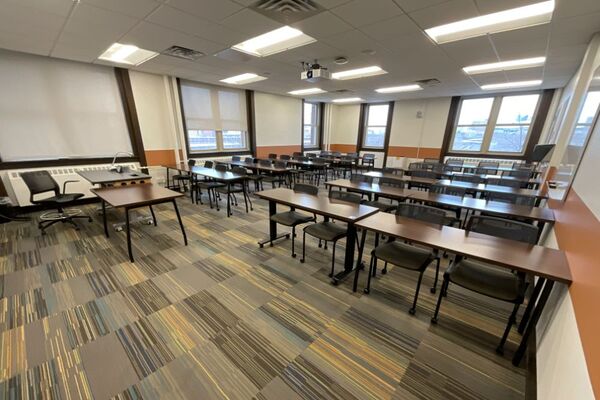 Back of room view of student table and chair seating and markerboard on right side wall of room