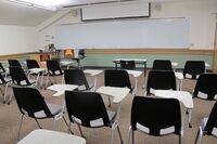 Front of room view with lectern on left in front of markerboard and projection screen partially raised