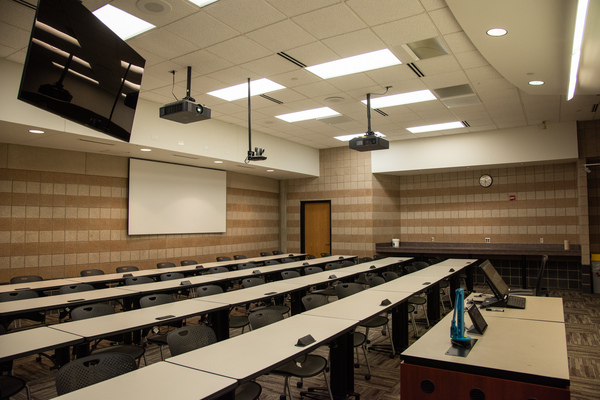 Instructor view from front left of classroom showing one confidence panel, rear projector display, audience seating, and front podium.