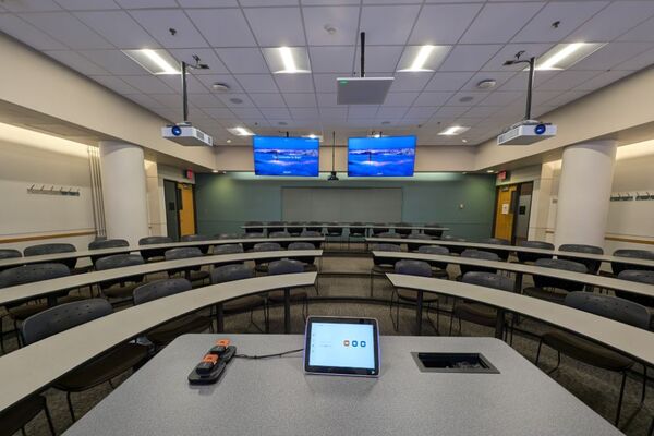 Back of room view of student tiered fixed-table and chair seating and exit doors at rear left and right of room